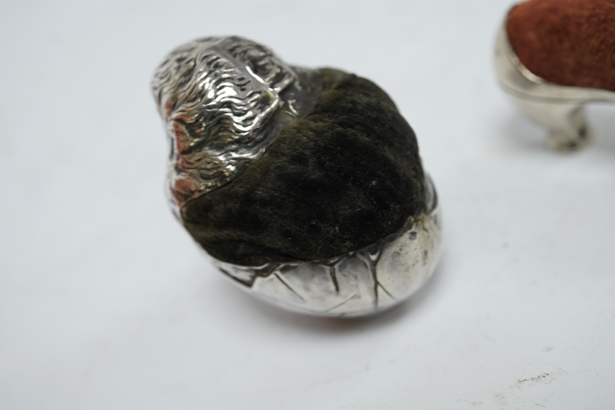 An Edwardian novelty silver pin cushion, modelled as a hatching chick, by Sampson Mordan & Co, Sheffield, 1906, height 43mm (hole), together with a late Victorian shoe pin cushion, by Adie & Lovekin, Birmingham, 1892, Co